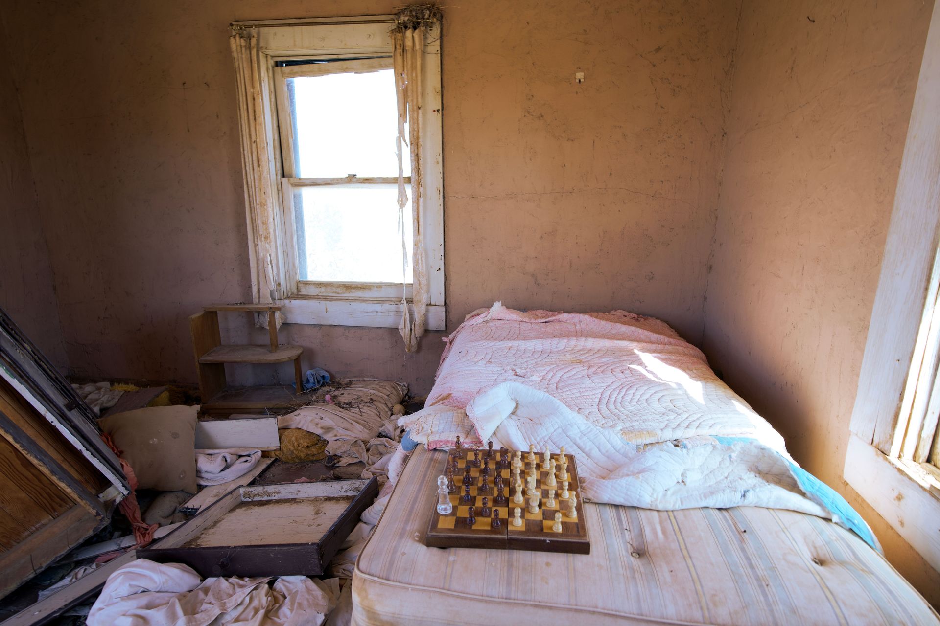 A desolate bedroom with unkempt bed and chessboard, conveying neglect.