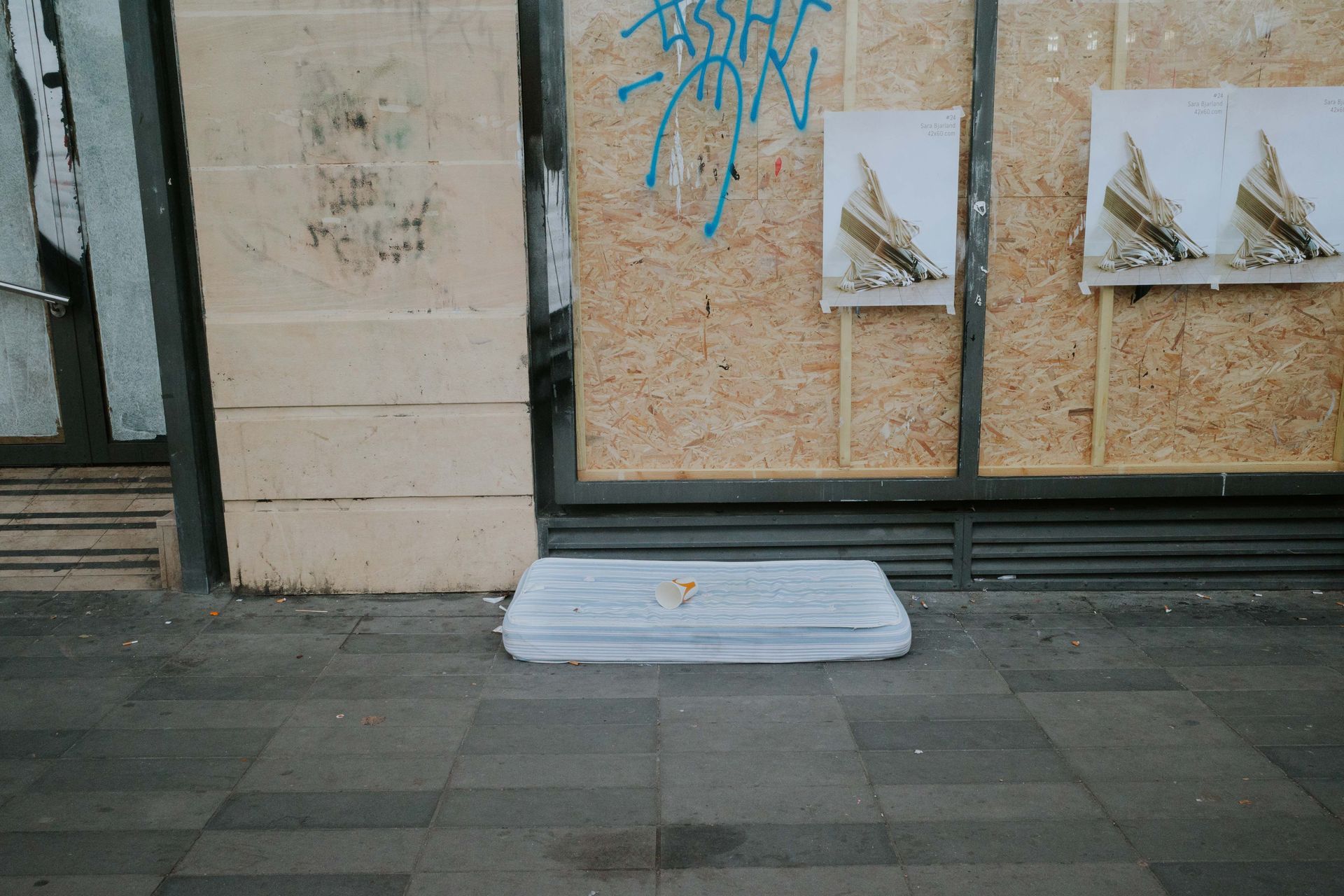 Image of an urban street with graffiti, a mattress, and discarded cup, conveying urban decay.